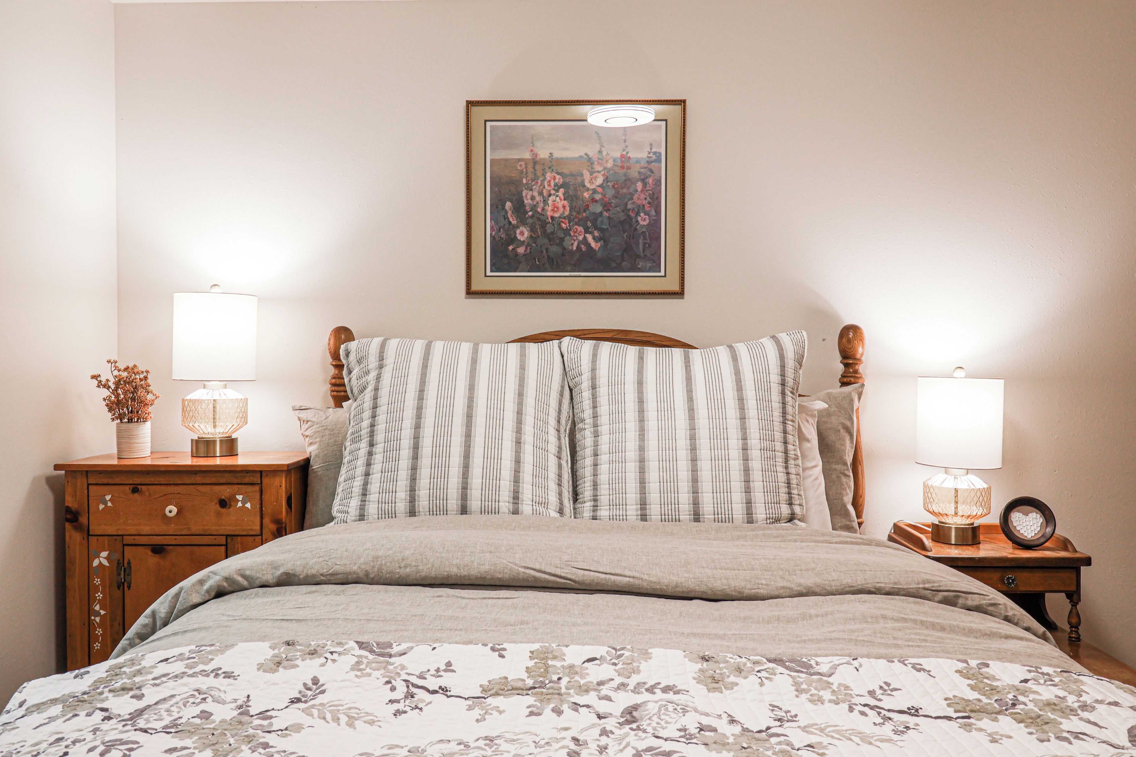 Una camera da letto con un letto, due comodini con lampade, un mobiletto e uno specchio, e un quadro appeso al muro.