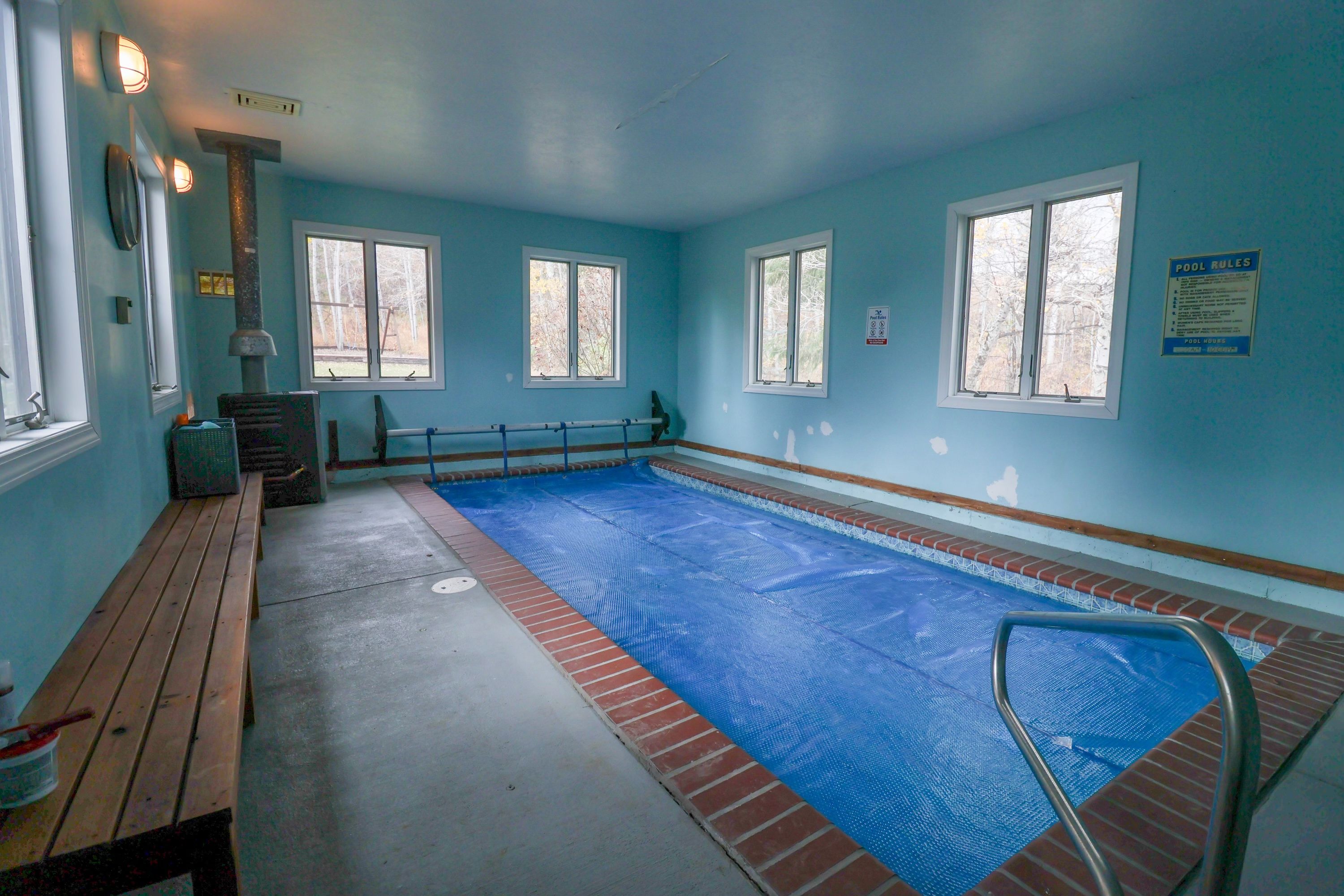 Una piscina con superficie d'acqua blu, circondata da un bordo in mattoni e dotata di trampolino e corrimano di sicurezza.