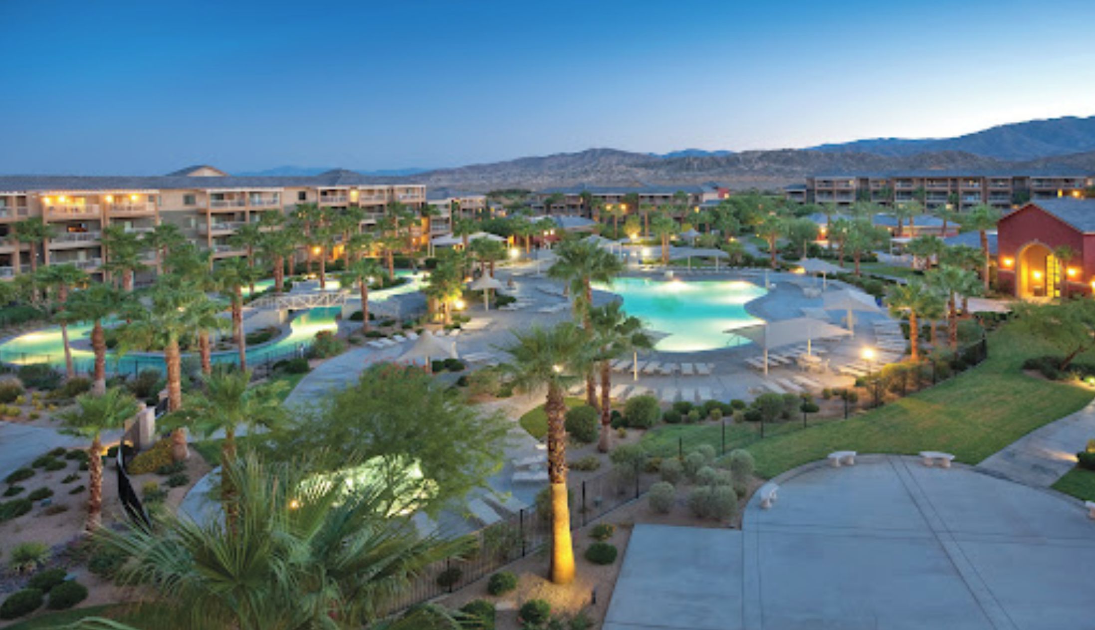 A resort with multiple swimming pools, palm trees, and a mountainous backdrop.