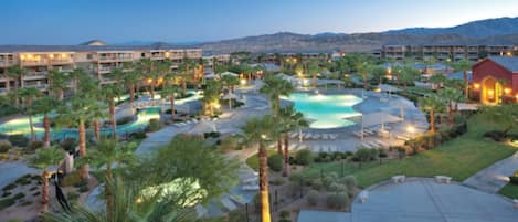 A resort with multiple swimming pools, palm trees, and a mountainous backdrop.