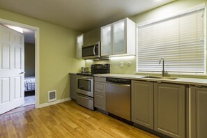 A compact kitchen with a microwave, oven, dishwasher, and a window with blinds. - Contemporary and Blinged-Out Private Guest Suite (Greeley)