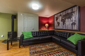 Ein Wohnzimmer mit einem schwarzen Ledersofa, einem kleinen Tisch, einer roten Akzentwand, einer Weltkarte und einem Kaminofen.