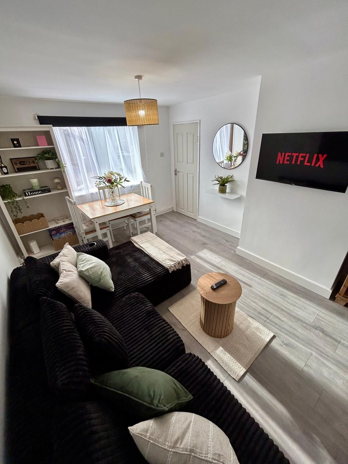 A modern living room with a black sectional sofa, a wooden coffee table, and a TV mounted on the wall.