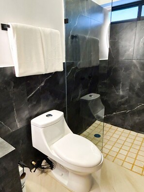 Et moderne badeværelse med toilet, glasbrusekabine og flisegulv.