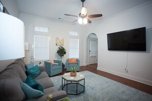 A living room with a gray sofa, teal armchairs, a coffee table, and a ceiling fan. - Gameday Home · Dog-Friendly · Private Lake (Bessemer)