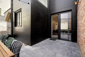 A modern building with a black exterior, a glass door entrance, and a patio area with outdoor seating. - Spacious Family Blankenberge House (Blankenberge)