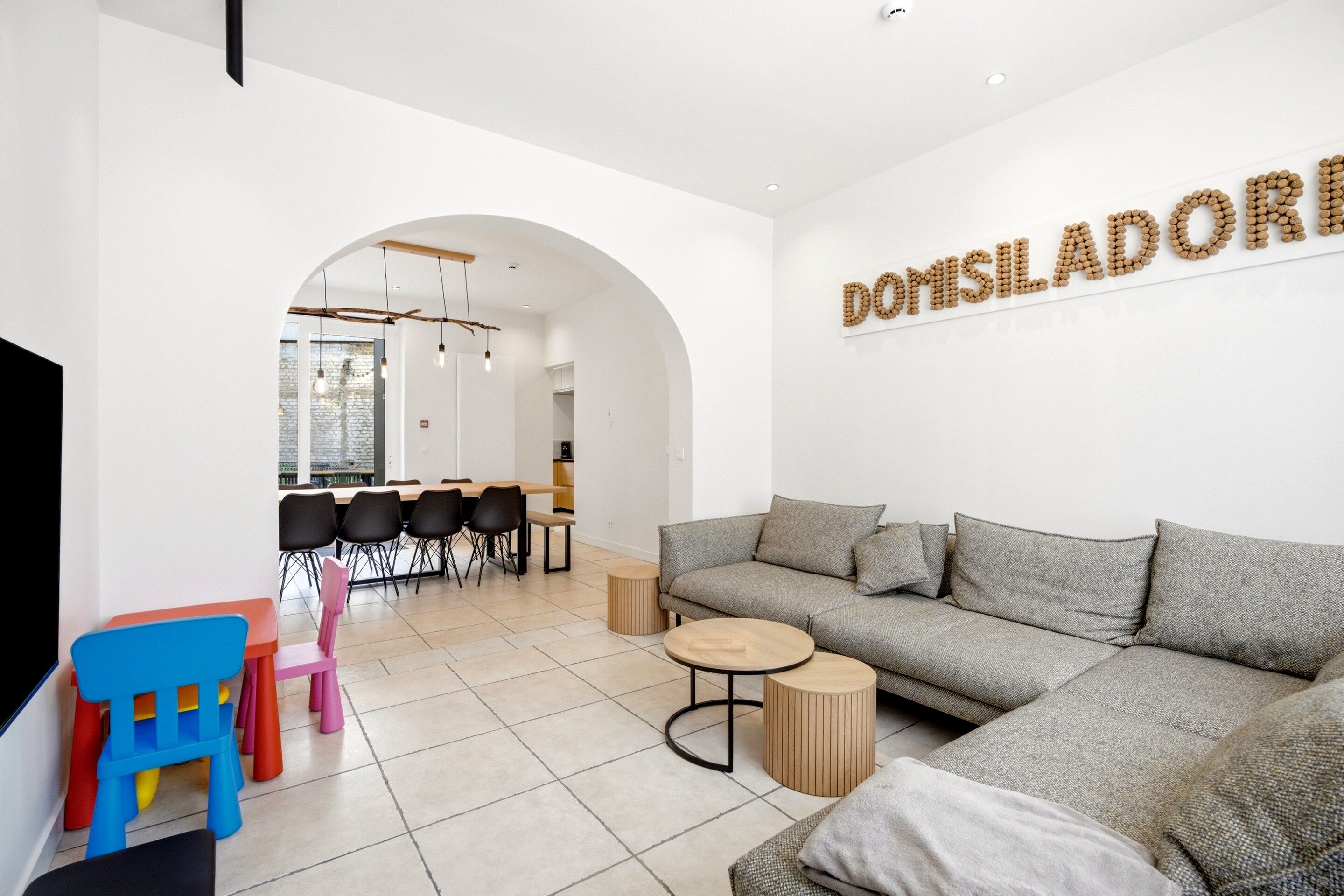 A modern living room with a grey sofa, a coffee table, and a dining area with chairs and a table.