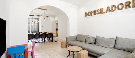 A modern living room with a grey sofa, a coffee table, and a dining area with chairs and a table.