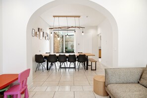 Ein moderner Essbereich mit einem langen Tisch und Stühlen, einem rundbogenförmigen Durchgang und einer Sitzecke mit einer Couch und einem kleinen runden Tisch.