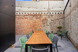 Eine Terrasse im Freien mit einem Holztisch und Stühlen, umgeben von Backsteinmauern und Lichterketten.