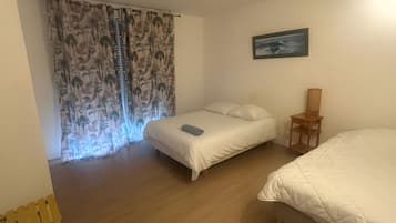 Ett sovrum med två sängar, ett trägolv, en tavla på väggen och en gardin med ett tropiskt mönster.