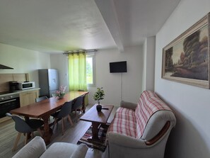 Ett kompakt bostadsutrymme med ett litet kök, en matplats, en soffa och en tv.