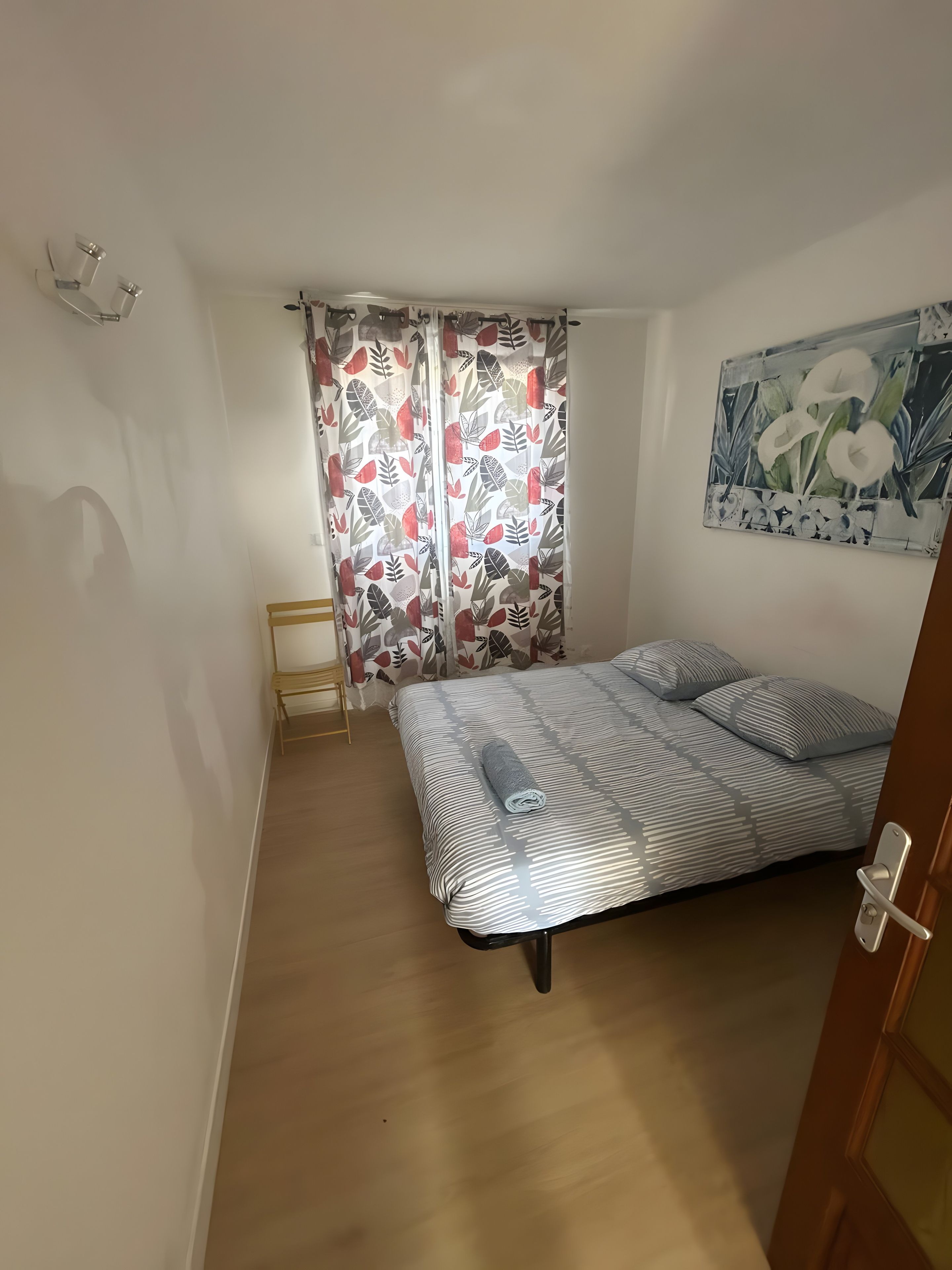 Ein Schlafzimmer mit einem Bett, einem Nachttisch, einem Fenster mit Vorhängen und einem Bild an der Wand.