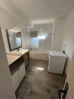 Ett litet badrum med handfat, spegel och en inbyggd tvättmaskin.