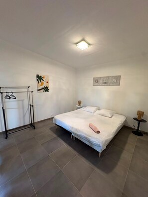 A bedroom with a bed, a hanging clothes rack, a wall-mounted artwork, and a small table with a lamp. - House 'Maison 10 personnes grande terrasse grands groupes' (Parcé)