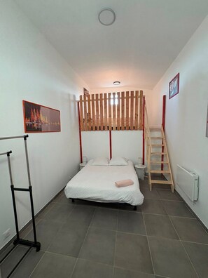 Habitación pequeña con literas, una escalera, una mesita y un radiador.