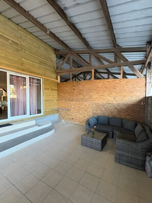 Un espacio al aire libre techado con pared de madera, un sofá y una mesa de vidrio.