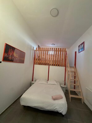 A bedroom with a bed, a wooden slat partition, a ladder, and a small table with a cup. - House 'Maison 10 personnes grande terrasse grands groupes' (Parcé)