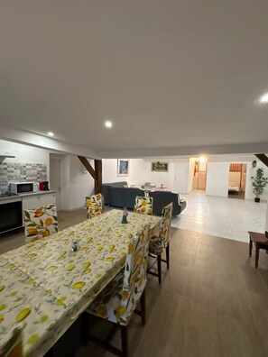 A spacious living area with a dining table, sofas, and a kitchen area with a microwave and toaster. - House 'Maison 10 personnes grande terrasse grands groupes' (Parcé)