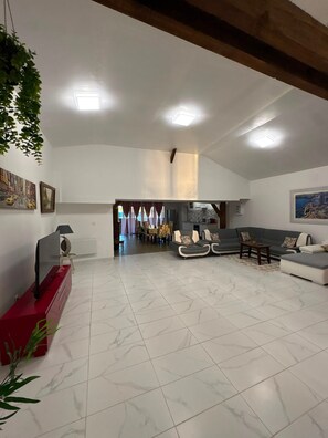 A spacious living area with a dining table, sofas, and a kitchen in the background. - House 'Maison 10 personnes grande terrasse grands groupes' (Parcé)