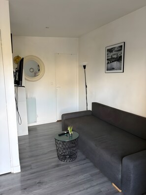 En moderne stue med en grå sofa, et rundt sofabord med en plante, en lampe og et billede i ramme på væggen.