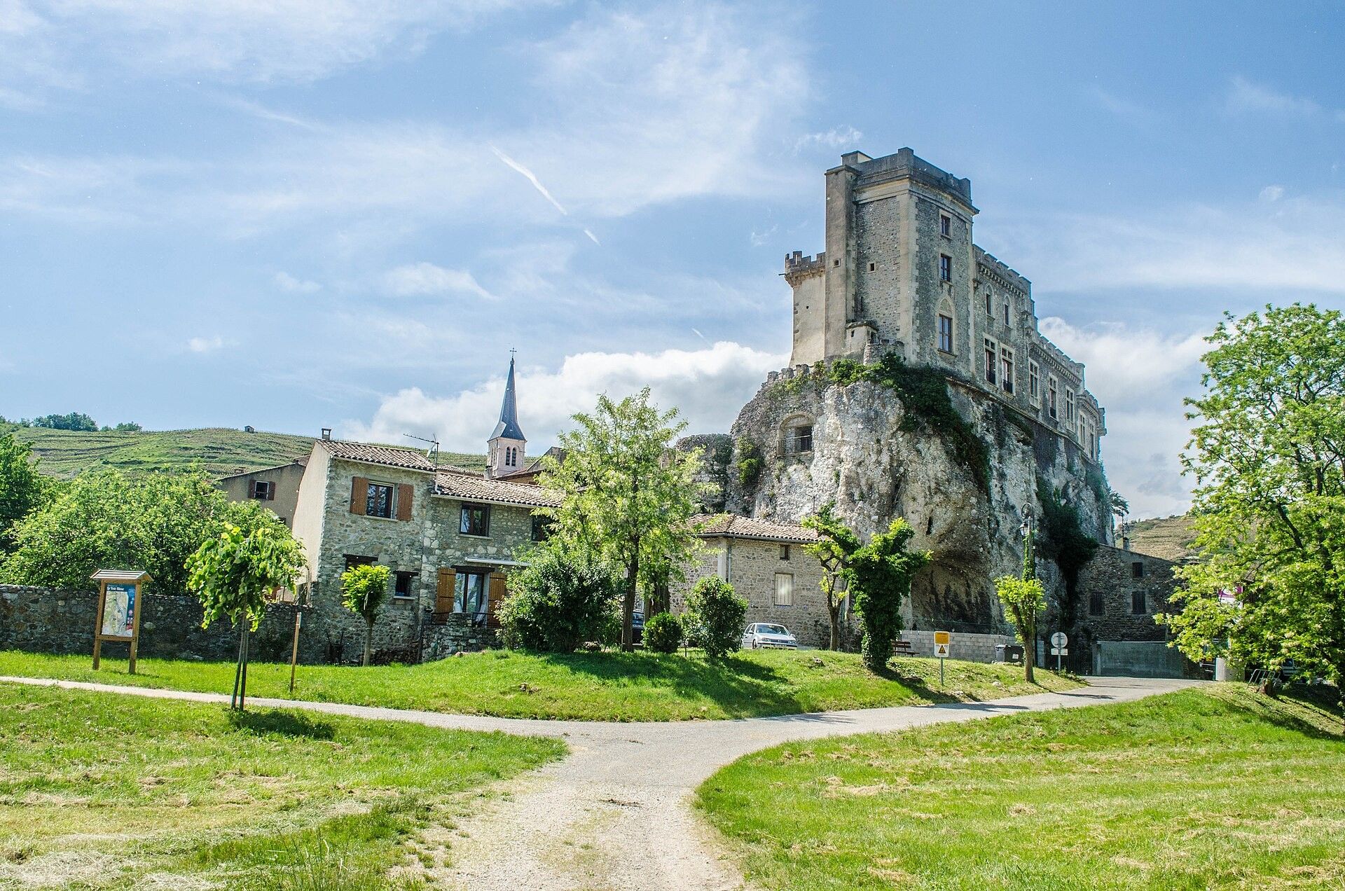 Ein historisches Steinhaus mit einem Turm, umgeben von einer grünen Wiese und einem gepflasterten Weg.