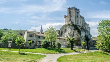 Ein historisches Steinhaus mit einem Turm, umgeben von einer grünen Wiese und einem gepflasterten Weg.