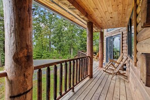 Une terrasse en bois avec une balustrade, un fauteuil à bascule et une porte vitrée donnant sur une zone boisée.