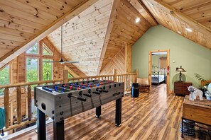 Un loft spacieux avec un plafond en bois, une table de baby-foot et une vue sur l’extérieur.
