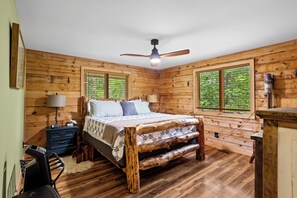 Ein Schlafzimmer einer Holzhütte mit einem Bett, Nachttischen, einem Schreibtisch und einem Deckenventilator.