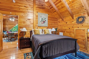 A wooden interior with a bed, nightstands, and a dining area. - Wildcat Cabin at Lake Lure (Lake Lure)