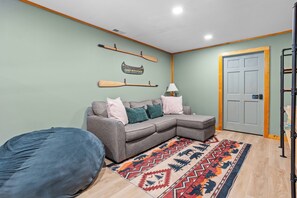 A living room with a sectional sofa, a patterned rug, and wall-mounted paddles. - Wildcat Cabin at Lake Lure (Lake Lure)