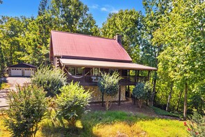 A wooden cabin with a red roof, surrounded by lush greenery and trees. - Wildcat Cabin at Lake Lure (Lake Lure)