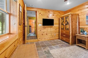 Interior de madera con un televisor montado en la pared, una mesita de mimbre y una puerta que da a otra habitación.