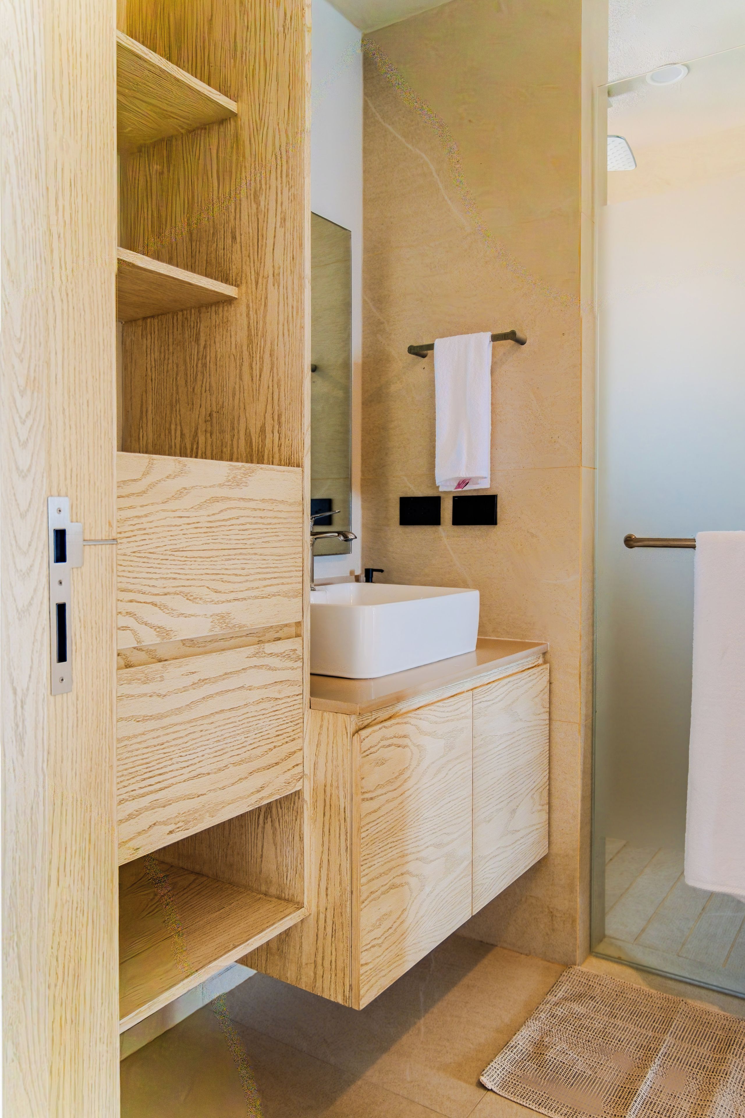 A modern bathroom with a wooden vanity, a white sink, and a glass shower enclosure.