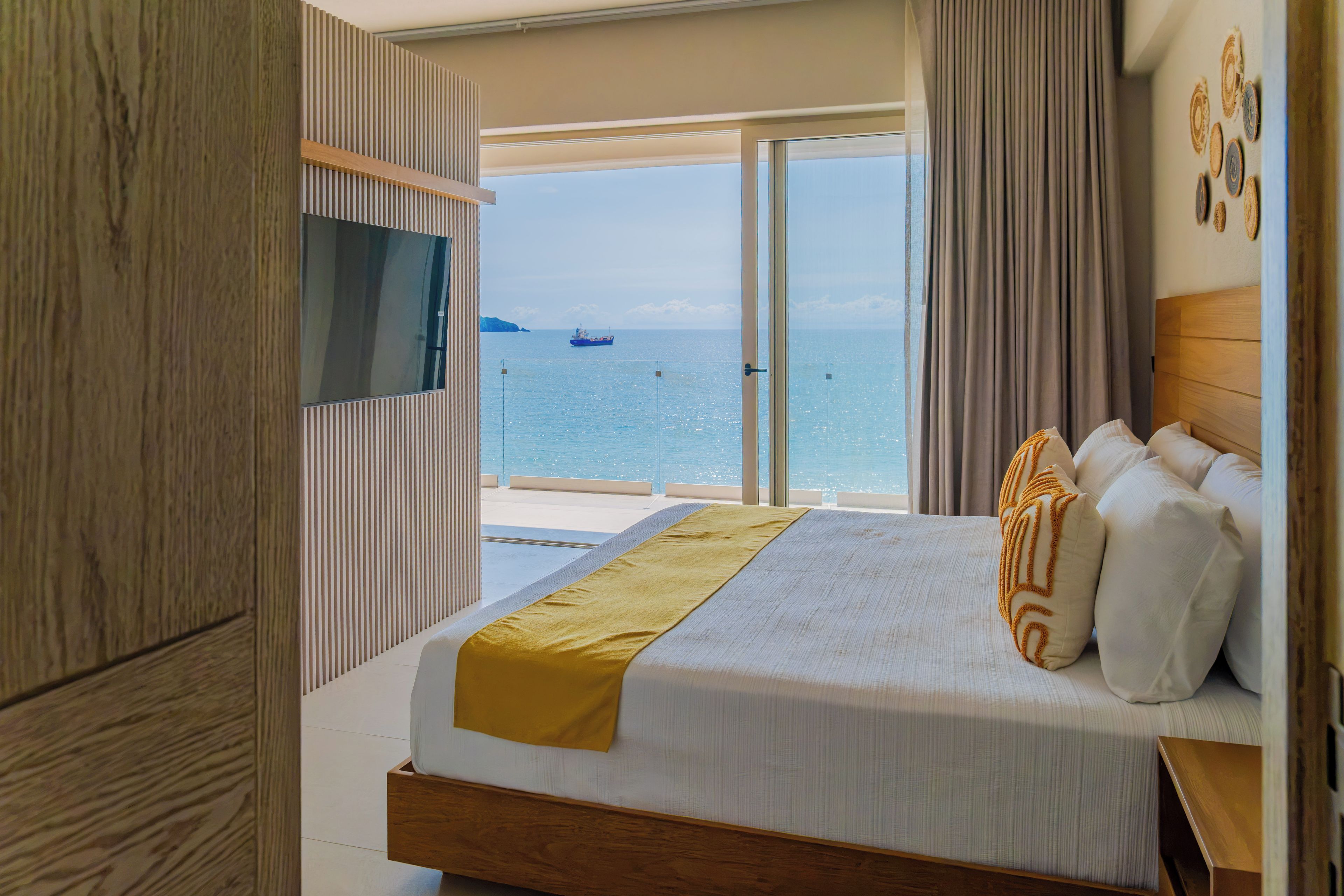 A hotel room with a bed, a television, and a view of the sea.