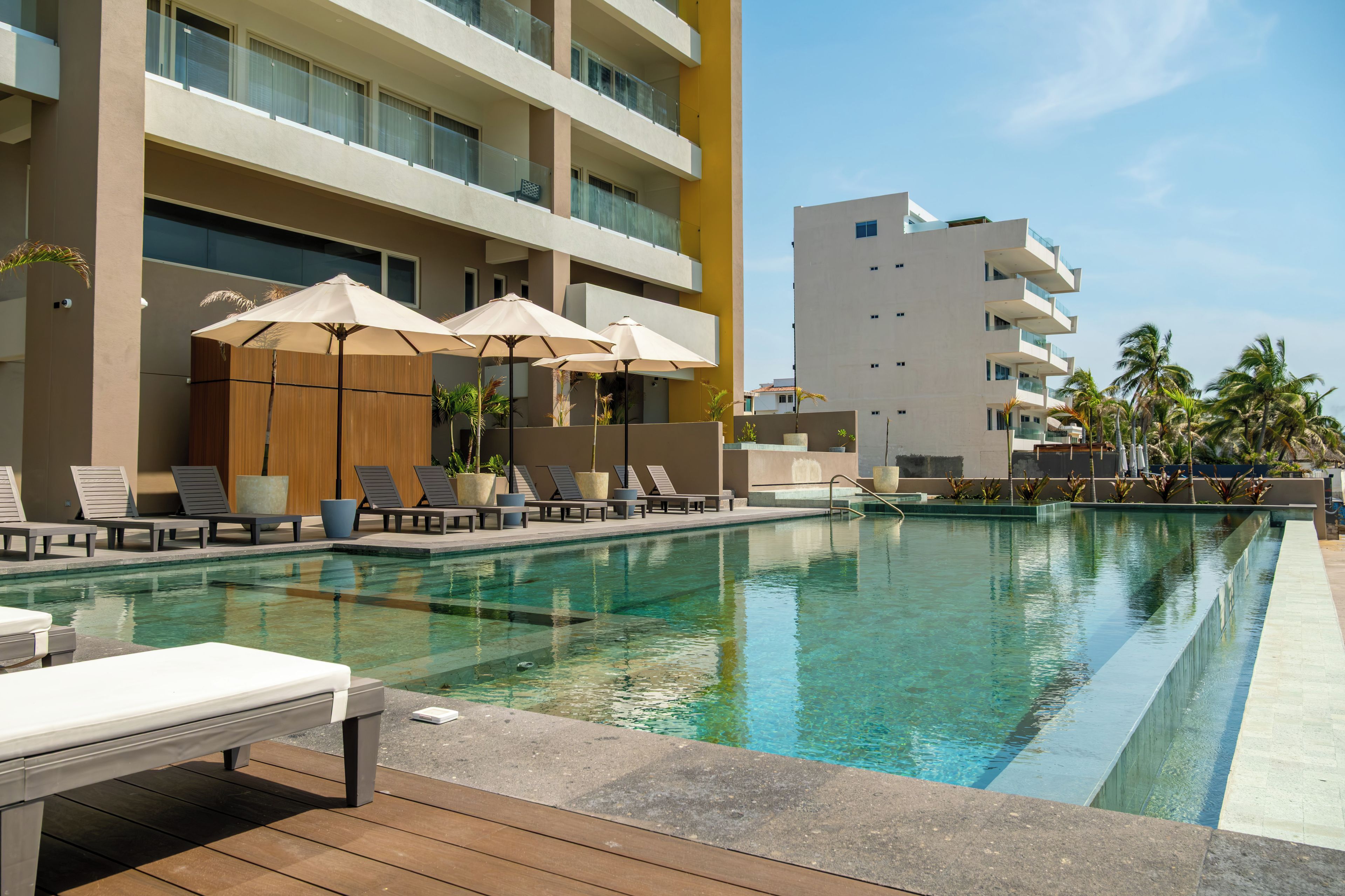 Zona de piscina moderna de hotel con tumbonas, sombrillas y agua cristalina.