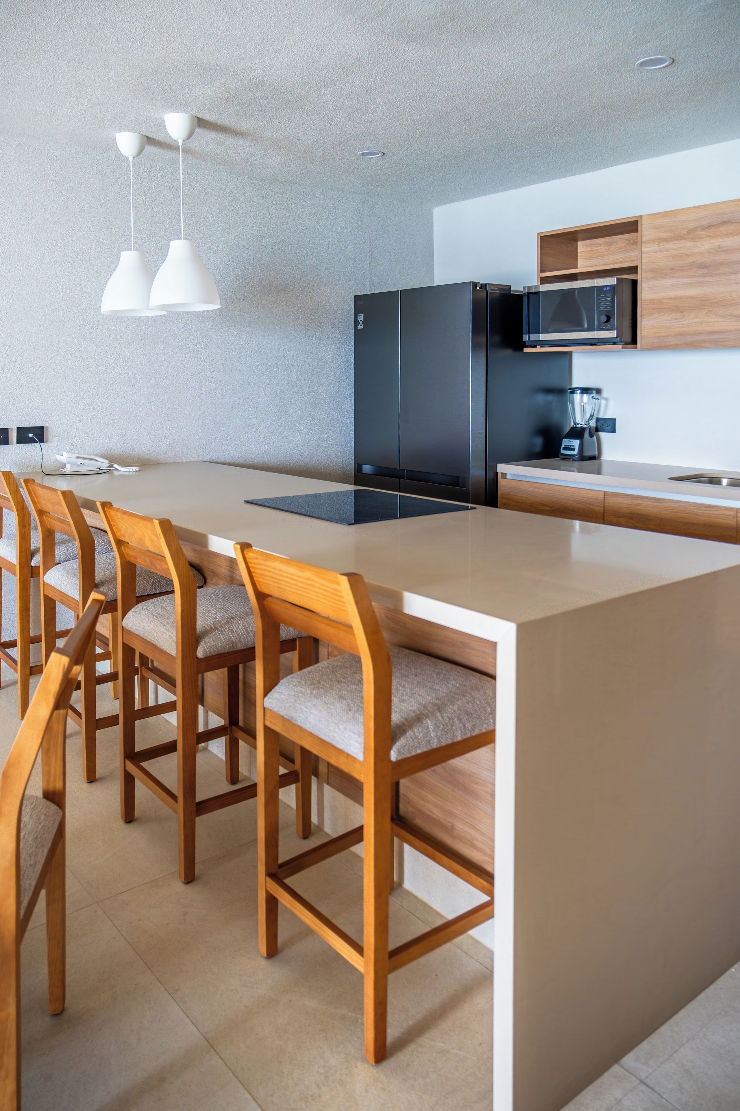 Une cuisine moderne avec un îlot central, des chaises en bois, un réfrigérateur noir et un four à micro-ondes.