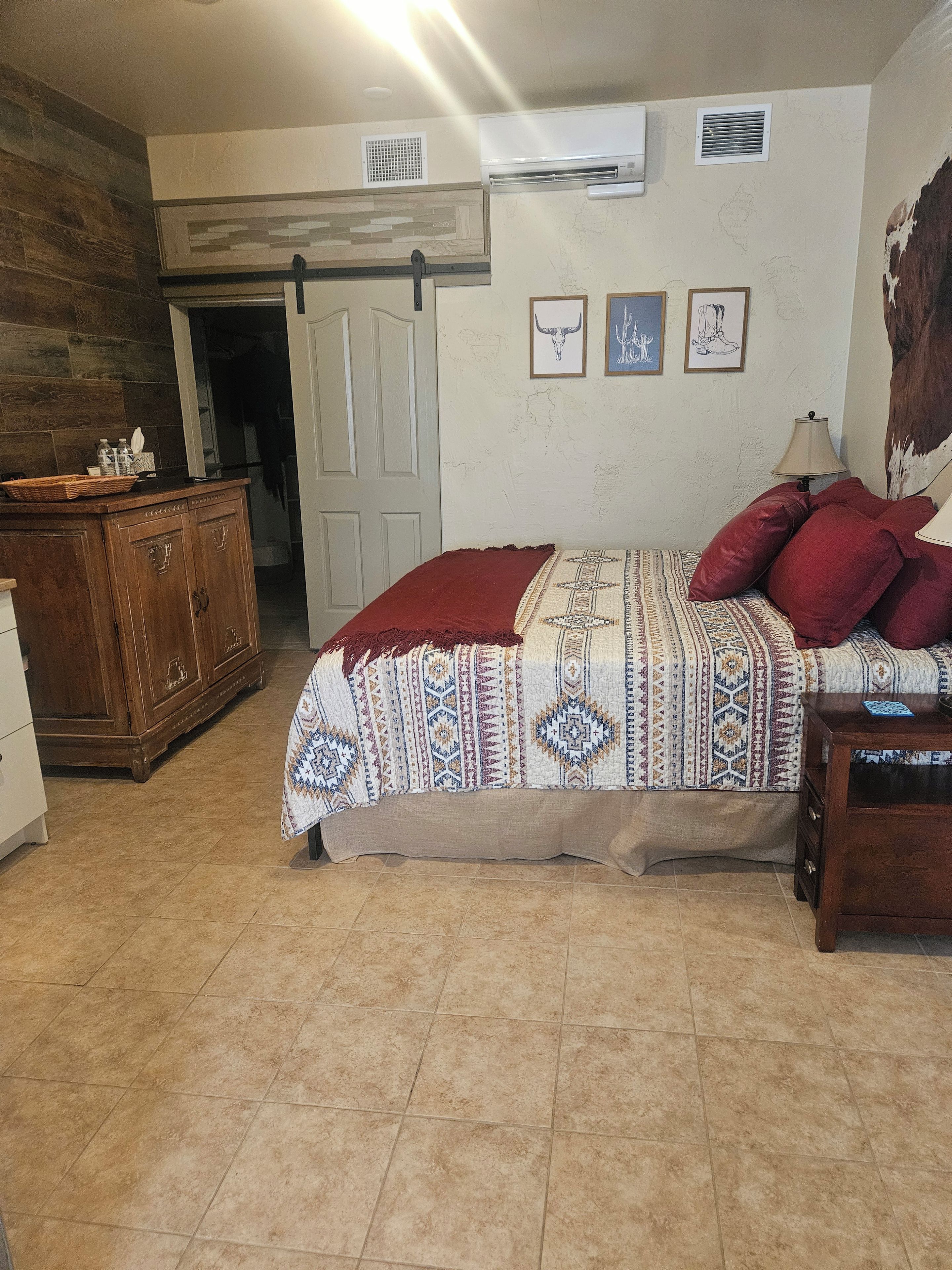 Quarto com cama, cómoda de madeira, porta e parede decorada com obras de arte.