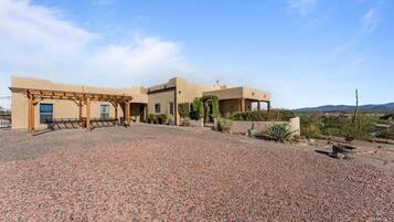 A building with a covered patio area, a gravel driveway, and a desert landscape in the background.