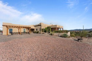 Un edificio con patio coperto, vialetto sterrato e paesaggio desertico sullo sfondo.