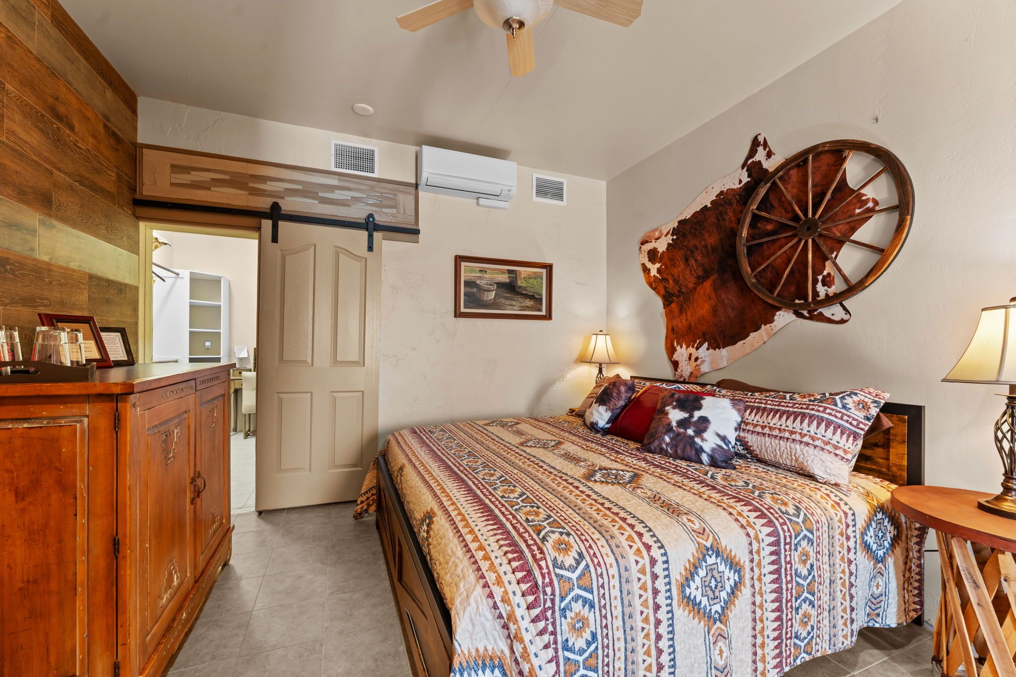 A bedroom with a bed, wooden dresser, and a wall-mounted cow hide.
