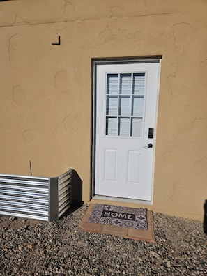 Una porta bianca con una finestra, un cancello metallico e un tappetino d'ingresso con la scritta 'HOME'.