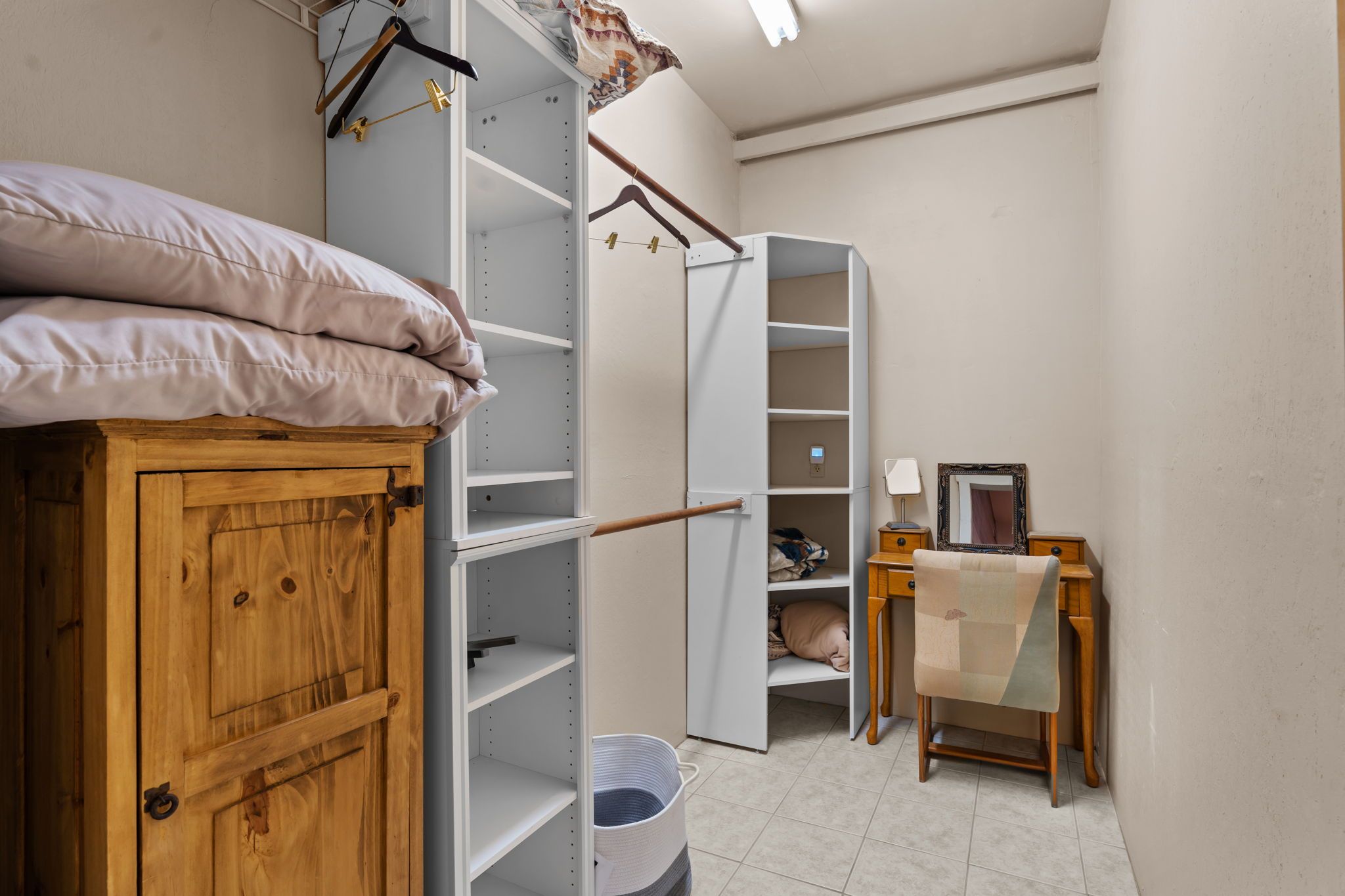 Ein Schlafzimmer mit einem Holzschrank, einem Bett mit Kissen, einem Kleiderschrank mit Ablagefläche, einem Nachttisch mit Lampe und einem Sessel.