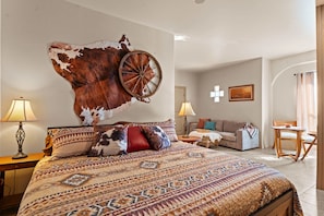 A spacious bedroom with a large bed, a wall-mounted wooden wheel, a sofa, and a small table.