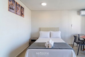 A hotel room with a bed, a nightstand, a chair, and a wall-mounted air conditioner. - Studio in Condo. w/ Pool and City View Msu0902 (Governador Valadares)