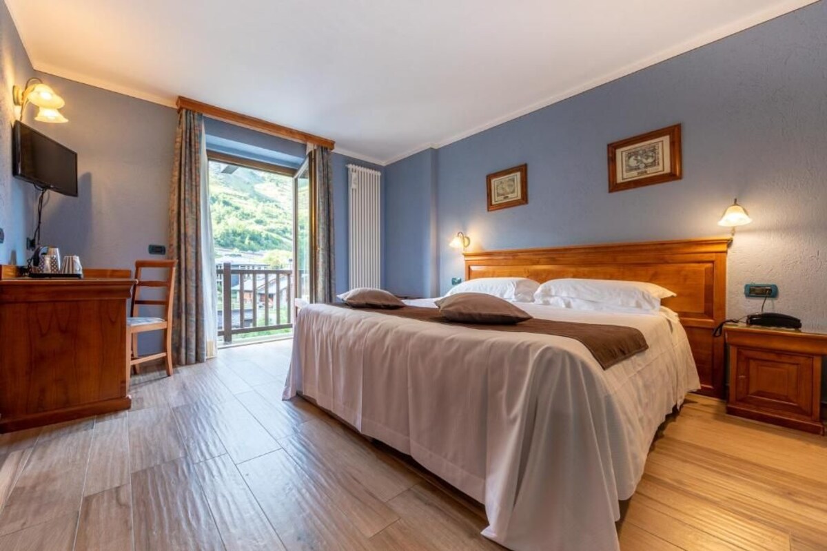 Un dormitorio con cama, mesitas de noche, televisor y vistas al exterior.