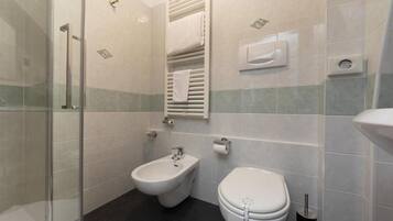 A bathroom with a glass shower enclosure, a bidet, and a toilet.