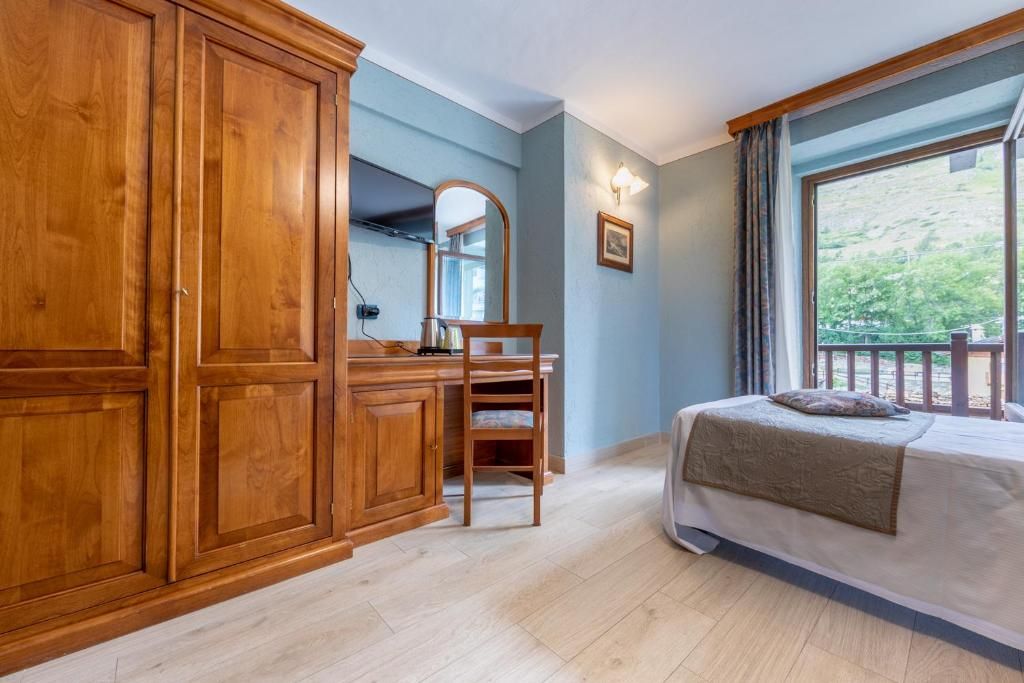 A bedroom with a bed, wooden wardrobe, desk, chair, and a window with a view.