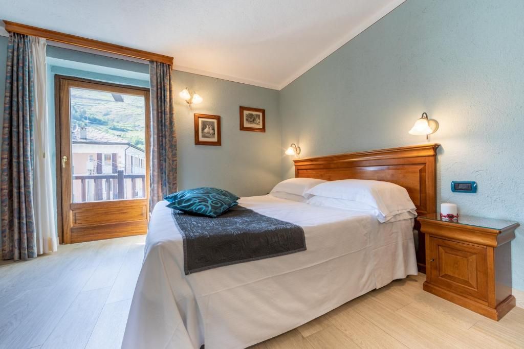A bedroom with a bed, a nightstand, a window with curtains, and a wall-mounted lamp.